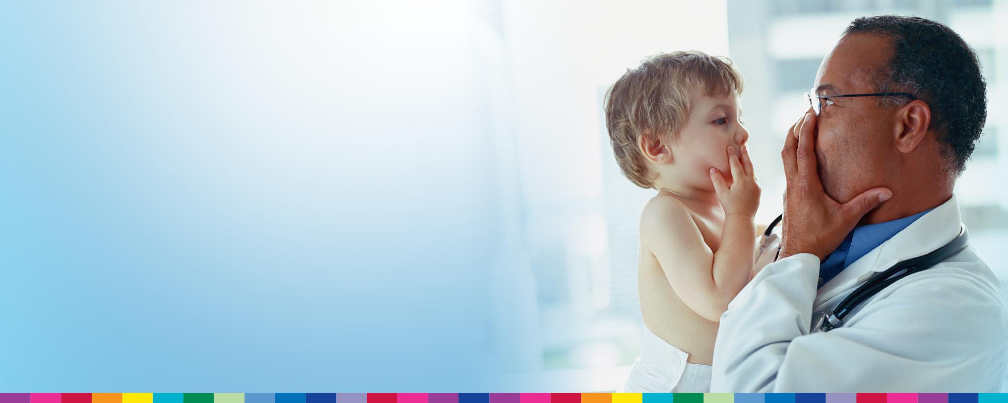 A doctor is holding a child and they are making playful faces at each other and smiling.