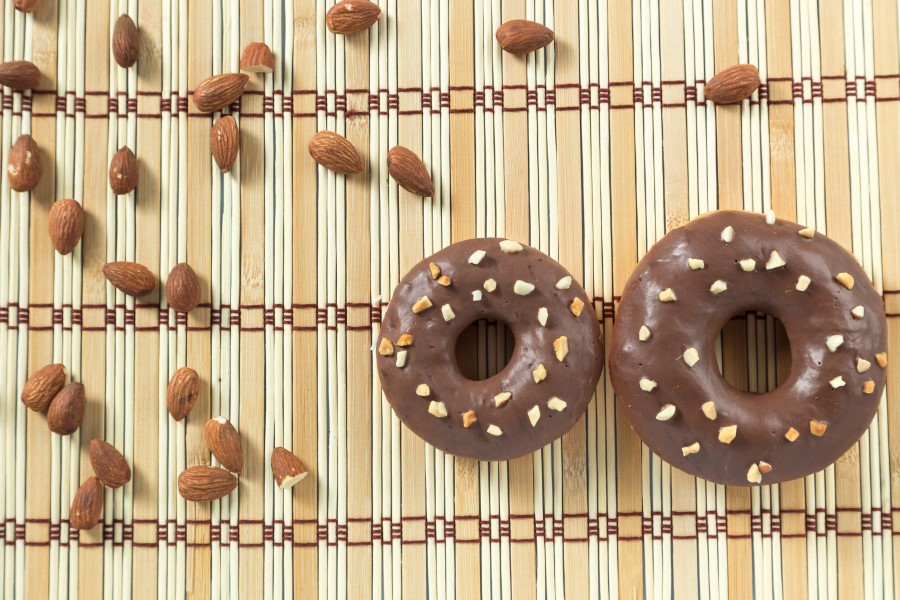 Two Avocado-Dark Chocolate Glazed Donuts with almonds on a bamboo placemat.