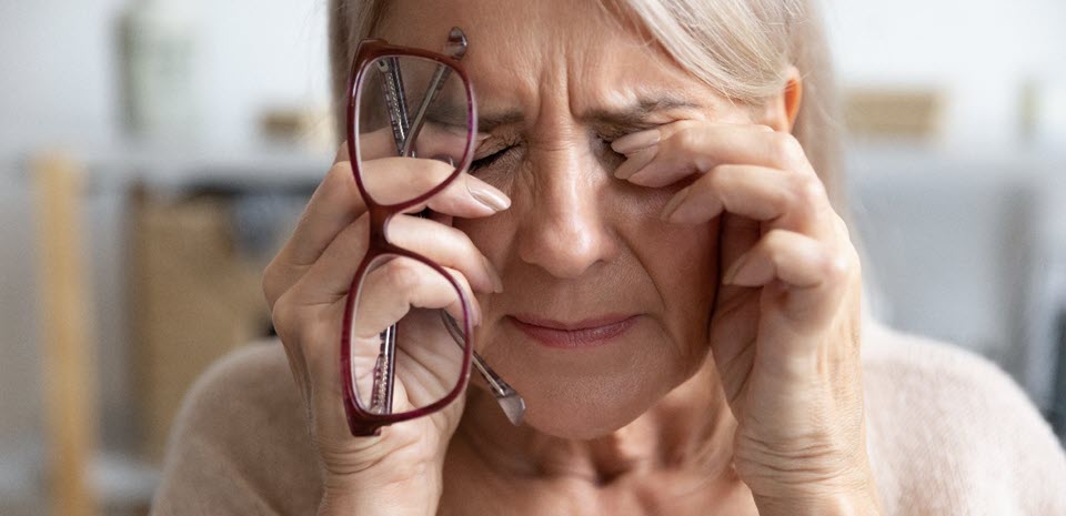 A mature woman holds her glasses and rubs her eyes.