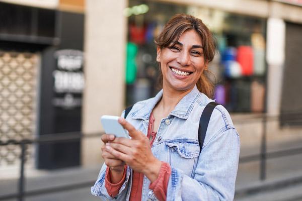 Una mujer sonríe mientras sostiene su teléfono, ahora que puede usar myChart en Español.