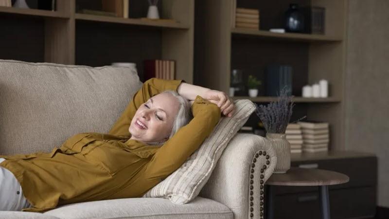 A serene woman practicing mindfulness while laying on a living room couch.