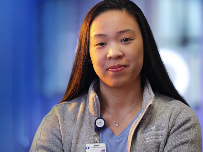 A close-up of an Asian-American UMass Memorial Health caregiver slightly smiling.