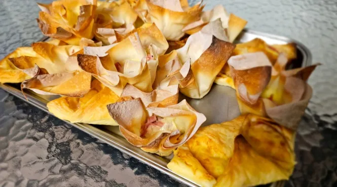 A tray featuring ham and cheese wontons on a table.