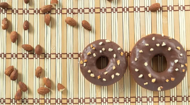 Two Avocado-Dark Chocolate Glazed Donuts with almonds on a bamboo placemat.