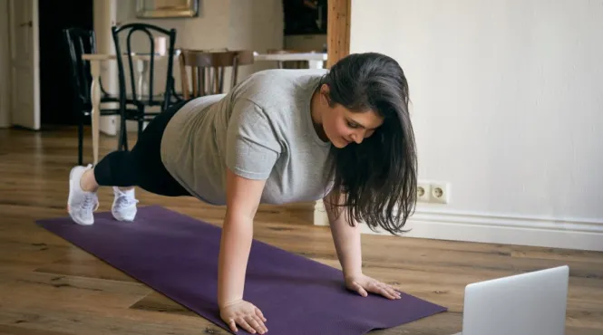 Woman concerned about spine health doing a plank in front of laptop