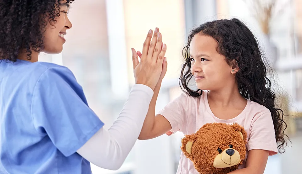 A health care worker and a child are doing a high five.