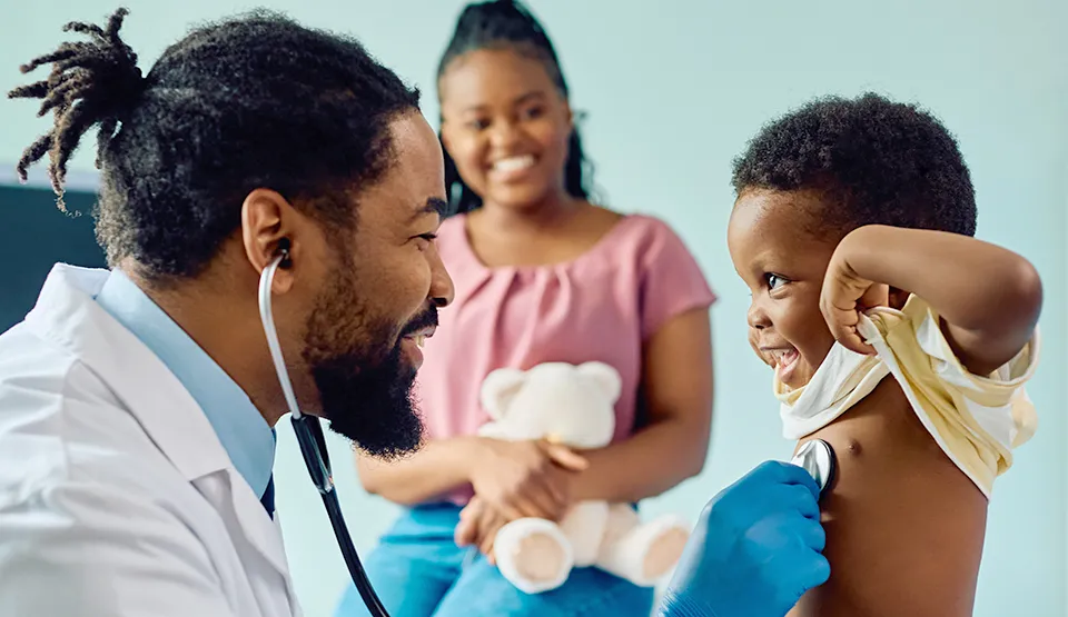 A doctor uses a stethoscope to examine a happy child's breathing, with the mother also present.  