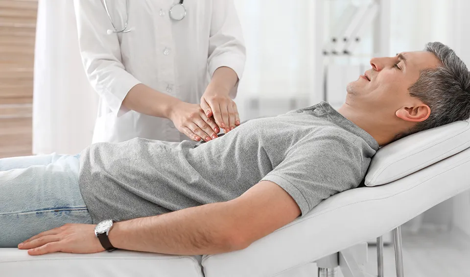 A doctor examines a patient's abdomen, pressing in a specific area.