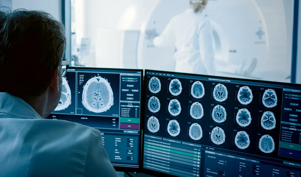 A man looks at a brain scan from the booth, during a patient's MRI.