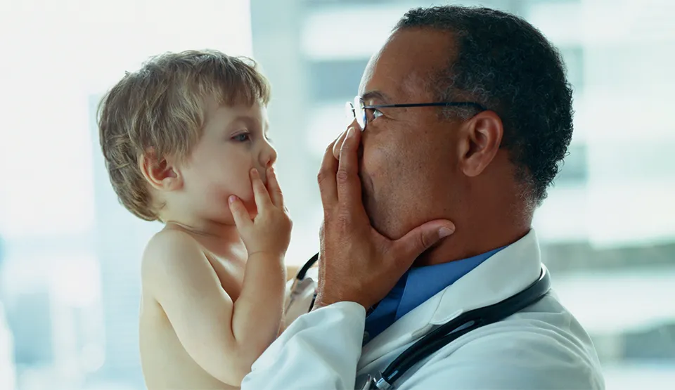 A doctor is holding a child and they are making playful faces at each other and smiling.