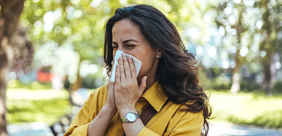 A woman in a park is holding a tissue to her nose.