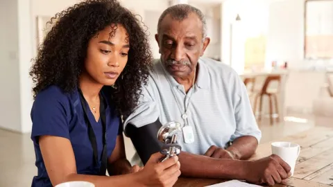 A nurse is taking a man's blood pressure in his own living room.