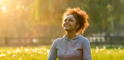 A woman sits in a sunny field appreciating nature and living in the present.