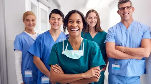 A group of confident and smiling nurses in a hospital hallway.