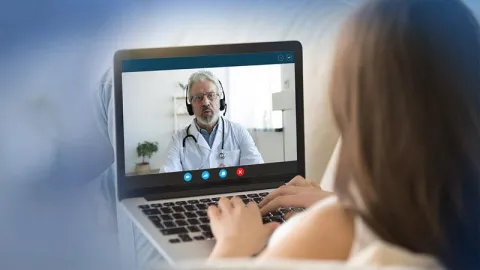 A woman is on a laptop talking to a doctor during a Telehealth visit.