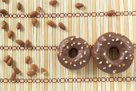 Two Avocado-Dark Chocolate Glazed Donuts with almonds on a bamboo placemat.