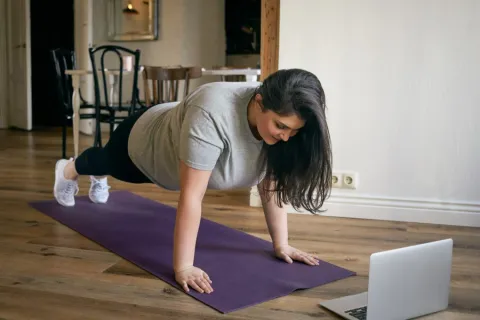 Woman concerned about spine health doing a plank in front of laptop