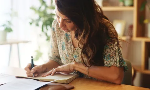 A woman sits at a desk, conducting research and taking notes.