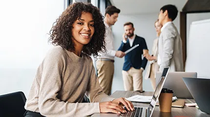 woman smiles at camera while working on computer