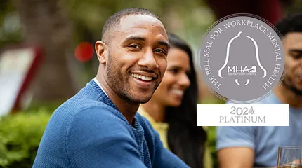 Man smiles at camera. A Bell Seal award for Workplace Mental Health is in the corner of the image