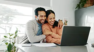 Husband and wife hug and smile while looking at their laptop