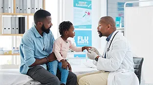 Doctor talks to little girl as she sits on father's knee