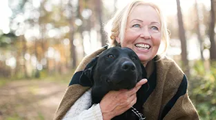 A woman cares for herself and her dog by walking in the woods.