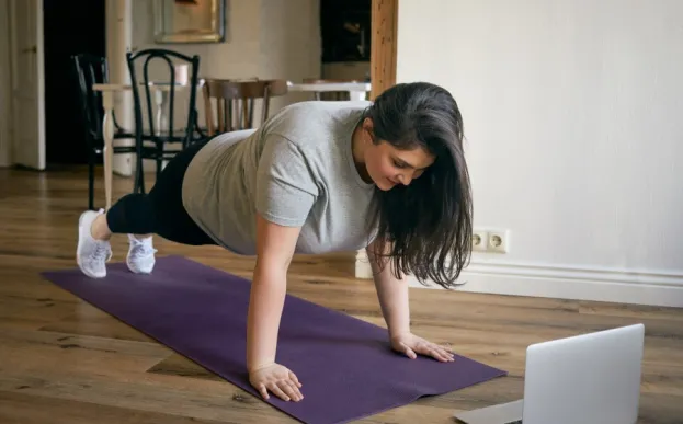 Woman concerned about spine health doing a plank in front of laptop